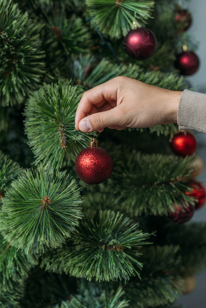 cropped image of man decorating christmas tree with red baubles at home - Fotografie, Obrázek
