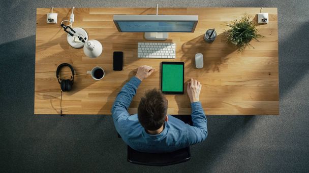 Вид сверху на человека, сидящего на рабочем столе. Мбаппе и смартфон с зеленым экраном лежат на столе
. - Фото, изображение