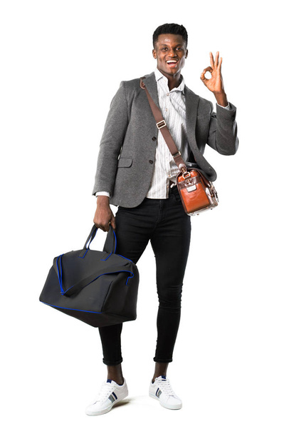 Corps complet d'homme d'affaires afro-américain voyageant avec des valises montrant un signe ok avec les doigts. Visage de bonheur et de satisfaction sur fond blanc
 - Photo, image