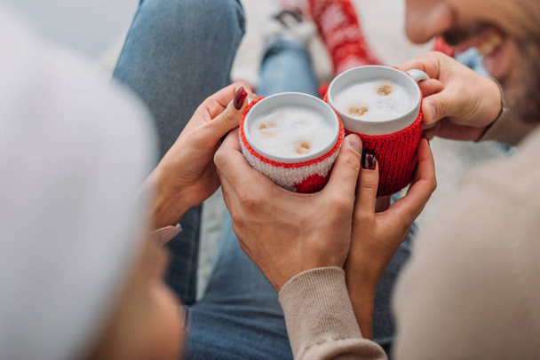cropped image of couple clicking with cups of cappuccino at home, christmas concept - 写真・画像