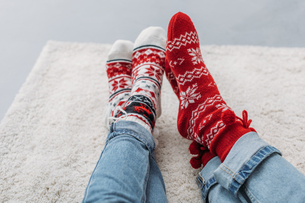 περικομμένη εικόνα ζευγάρι κάθεται στο χαλί με τζιν και Χριστουγεννιάτικες κάλτσες - Φωτογραφία, εικόνα
