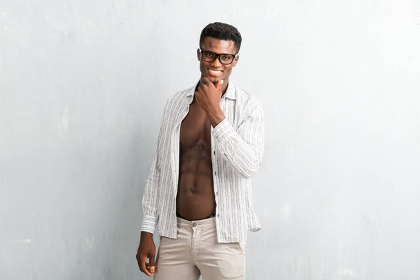 Young afro american man with glasses posing on textured grey wall - 写真・画像