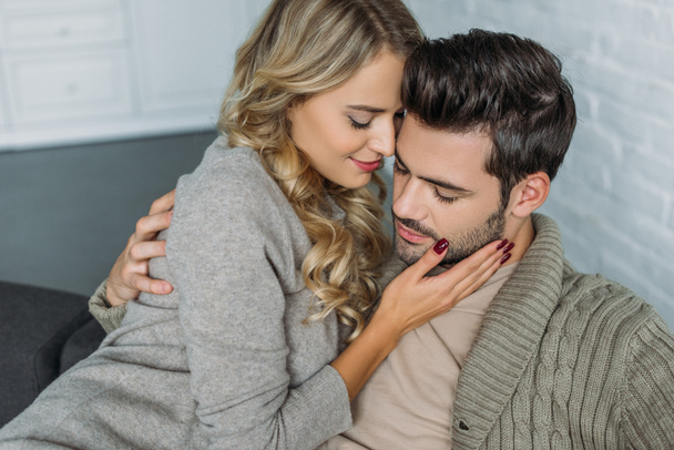 sorrindo jovem mulher abraçando seu namorado no sofá em casa
 - Foto, Imagem