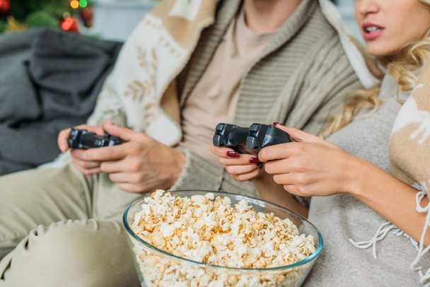 cropped shot of couple with popcorn playing video games together on couch at home - Photo, Image