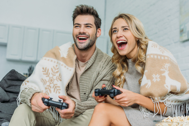beautiful young couple playing video games and having fun together on couch at home - Photo, Image