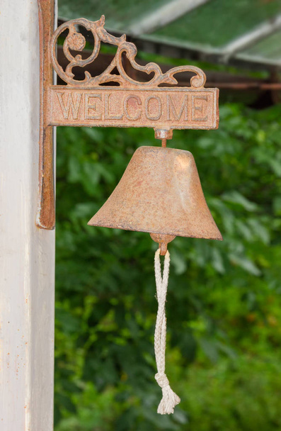 Stare antyczne dzwonek żelaza z przewodu na klapy dzwon na oddanych ażurowe wiszące i słowo Zapraszamy na nim na niewyraźne tło zielony - Zdjęcie, obraz