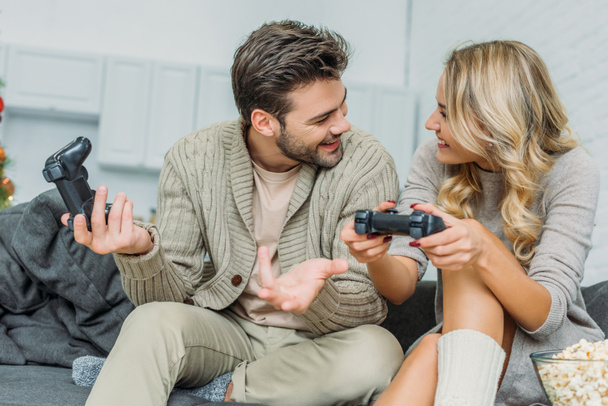 счастливая молодая пара играет в видеоигры вместе на диване дома
 - Фото, изображение