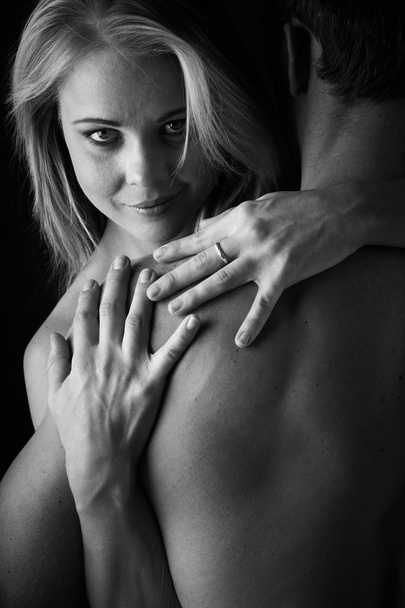 Young and fit caucasian adult couple in an embrace. Semi-nude and topless against a dark background. Black and White . - Foto, Imagem