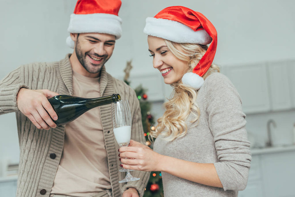 happy young couple pouring champagne into glasses in front of christmas tree at home - Foto, imagen