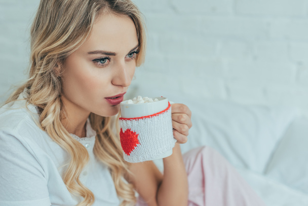 beautiful young woman drinking cocoa with marshmallow in bed at home - Photo, Image