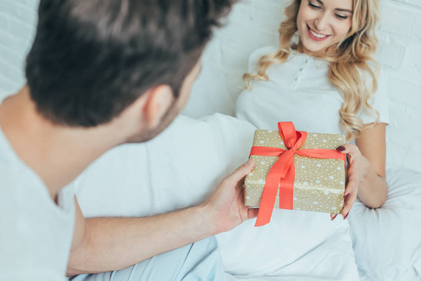 colpo ritagliato di giovane uomo che presenta regalo alla fidanzata a letto a casa
 - Foto, immagini