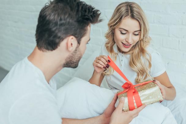 bel giovane uomo che presenta regalo alla fidanzata a letto a casa
 - Foto, immagini