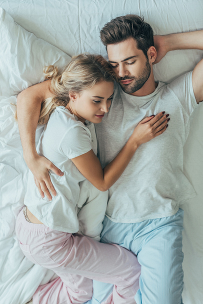 pohled shora na krásný mladý pár spolu vyspí a objímat v posteli doma - Fotografie, Obrázek