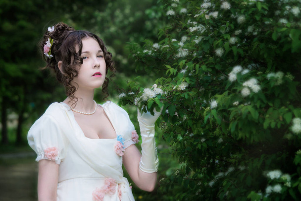 young girl in an elegant long white bride dress near blooming bush in a spring garden. - Foto, afbeelding
