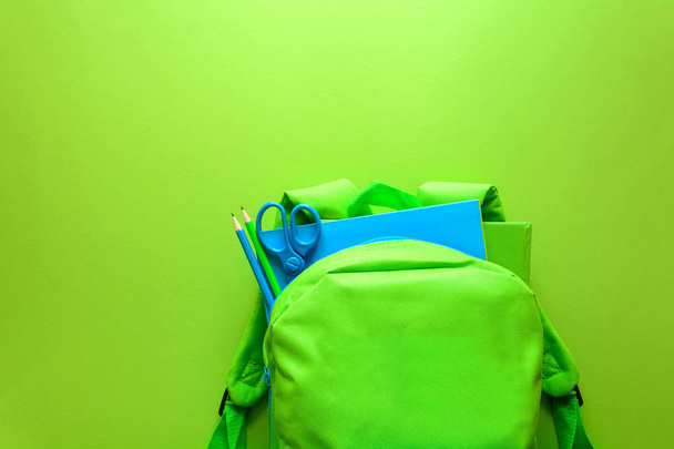 Back to school concept. Green backpack with school supplies on green background. Top view. Copy space - Foto, Bild