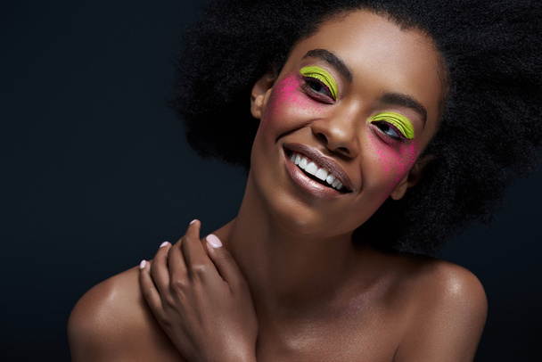 portrait of smiling african american model with bright neon makeup posing isolated on black - Foto, imagen
