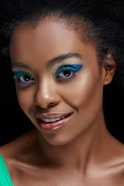 πορτρέτο του όμορφη αφρικανική αμερικανική μοντέλο με λαμπερά μπλε μάτια σκιές απομονωμένες σε μαύρο - Φωτογραφία, εικόνα