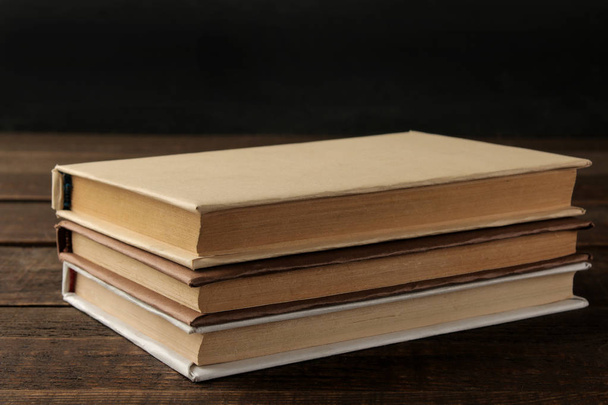 Una pila de libros sobre una mesa de madera marrón y sobre un fondo negro. Libros viejos. Educación. la escuela. estudio
 - Foto, imagen