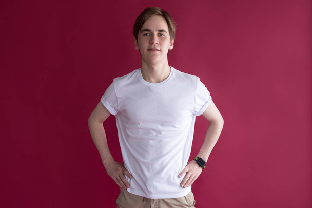 Young man in a white t-shirt is standing on a red background. Mock-up. - Foto, Imagem