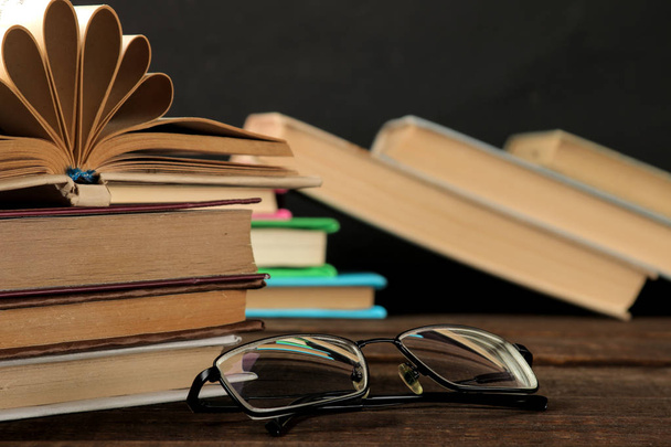 Пачка книг и стаканов на коричневом деревянном столе и на черном фоне. Старые книги. Образование. В школу. исследование
 - Фото, изображение