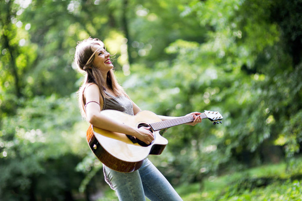 Beautiful woman playing acoustic guitar in nature - Zdjęcie, obraz