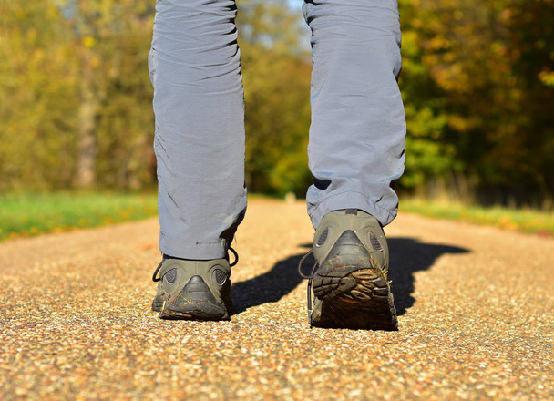 Ένας άνδρας περπατά κατά μήκος μιας διαδρομής χαλίκι σε μια ηλιόλουστη φθινοπωρινή μέρα - Φωτογραφία, εικόνα