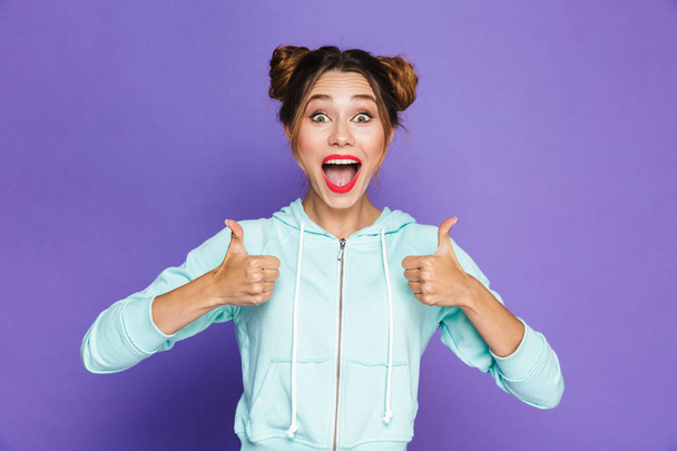 Portrait of excited woman with two buns shouting and showing thumbs up meaning good result or choice isolated over violet background in studio - Fotó, kép