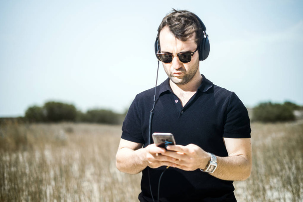 Pohledný mladý muž, přehrávání hudby ze svého smartphonu na jeho sluchátka - Fotografie, Obrázek