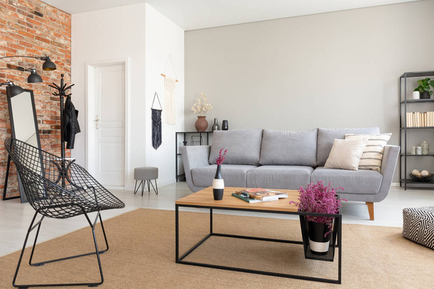 Modern armchair next to wooden table in living room interior with grey sofa and flowers. Real photo - Fotoğraf, Görsel