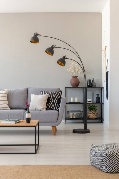 Black industrial lamp next to couch with patterned pillows in monochromatic living room, real photo with copy space on the wall - Φωτογραφία, εικόνα