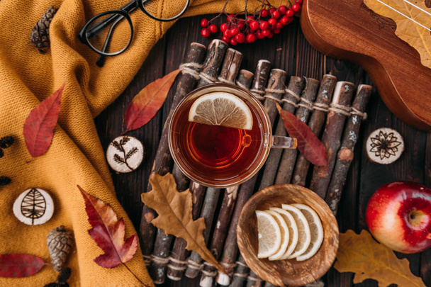 Flat lay. Textured scarf with cup of tea . Autumn leaves on wooden background . Autumn or Winter concept. - Фото, изображение