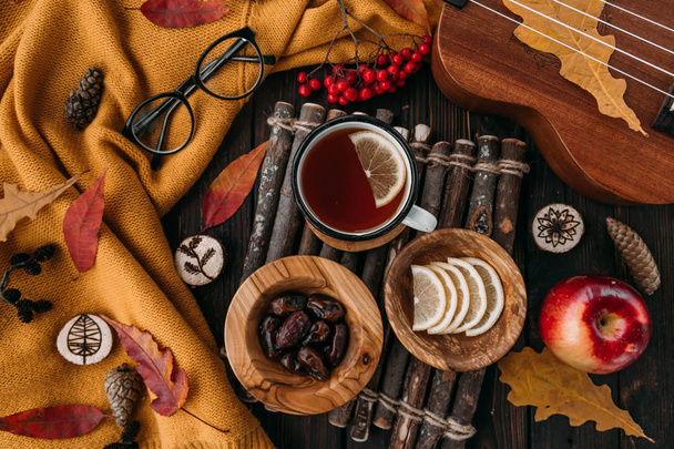 Flat lay. Textured scarf with cup of tea . Autumn leaves on wooden background . Autumn or Winter concept. - Фото, зображення