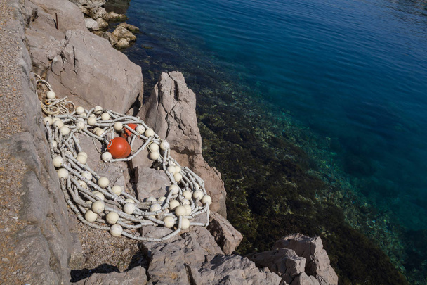 Água limpa e límpida do mar Adriático, com fundo visível. Rochas na costa, onde está uma corda com bóias. Omisalj, ilha Krk, Croácia
. - Foto, Imagem