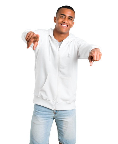 Dark-skinned young man with white sweatshirt points finger at you while smiling on isolated white background - Valokuva, kuva