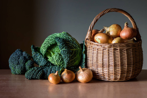 Bio zöldség - kelkáposzta, a brokkoli és a golden hagyma egy kosárban a fából készült asztal. Készlet-ból különböző fajta zöldség. - Fotó, kép