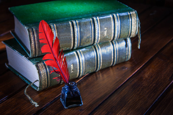 Kırmızı tüy kalem ve eski kitaplar ile ahşap bir masa üzerinde karanlık Inkwell - Fotoğraf, Görsel