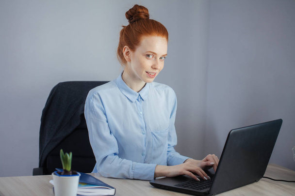 Portrait of redhaired young woman with laptop sitting at the tab - Foto, Bild