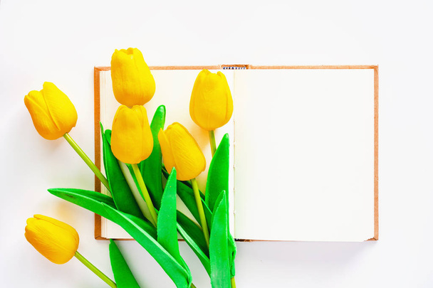 Artificial yellow tulips with blank notebook on white background for workspace, nature decoration and springtime concept - Foto, Imagem