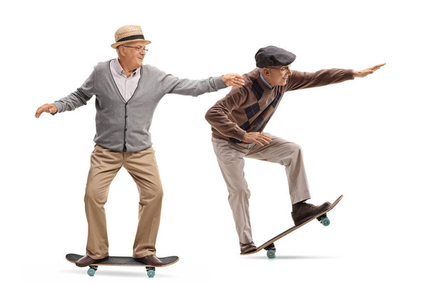 Full length profile shot of two elderly men skateboarding isolated on white background - 写真・画像
