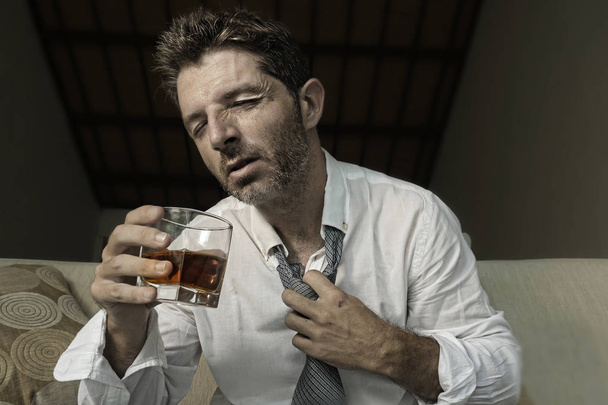 young attractive sad and desperate drunk addict businessman at home sofa couch drinking holding whiskey glass feeling depressed in alcohol addiction alcoholism problem and depression - Foto, immagini