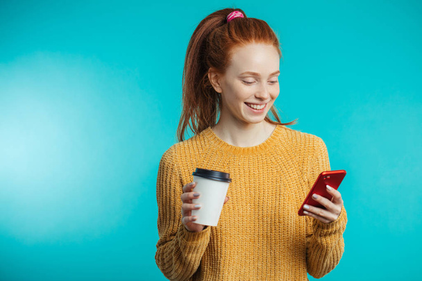 Young redhaired woman with coffee and smartphone isolated over b - Fotografie, Obrázek