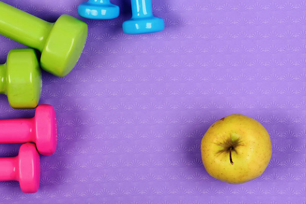 Barbells in pink, green and blue colors near apple fruits - Foto, immagini
