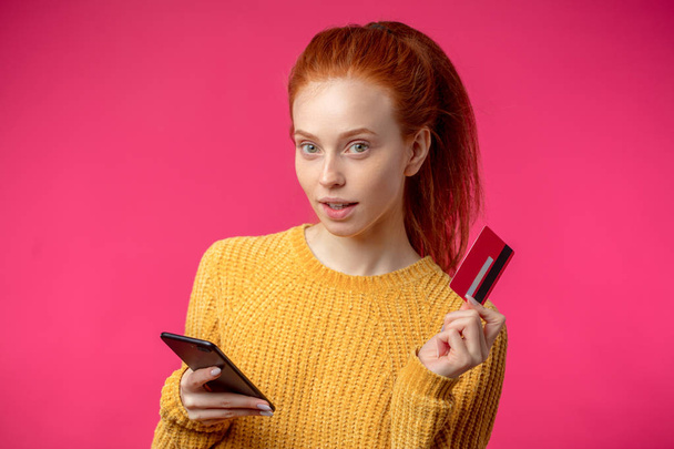 Portrait of cute ginger girl using smartphone isolated on pink background - Photo, Image