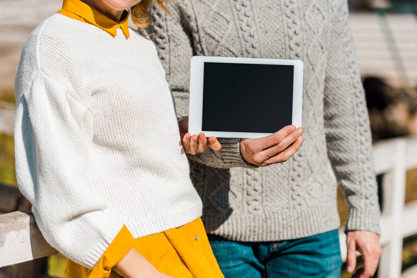 abgeschnittenes Bild eines Bauernpaares, das ein digitales Tablet mit leerem Bildschirm in der Nähe eines Holzzaunes auf einem Bauernhof zeigt - Foto, Bild