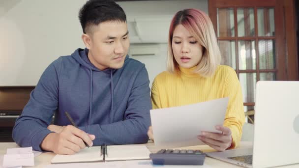 Jeune couple asiatique gérer les finances, l'examen de leurs comptes bancaires à l'aide d'un ordinateur portable et calculatrice à la maison moderne. Femme et homme faisant de la paperasserie ensemble, payer des impôts en ligne sur ordinateur portable
. - Séquence, vidéo