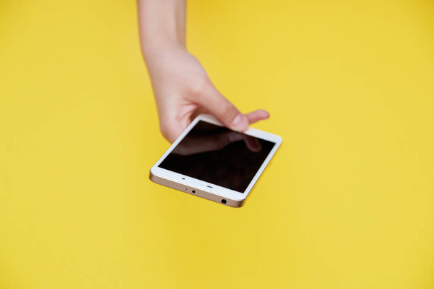 smartphone in hand on yellow background with copy space on top. - Фото, изображение