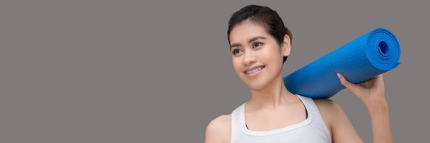 Young asian woman holding her yoga mat and charming smile while go to practice yoga exercise at the yoga sport gym.Photo design in banner cover size with copy space for add text. - Foto, imagen