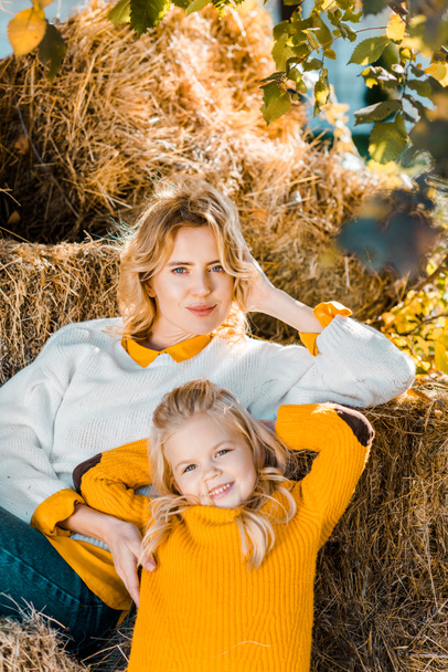 beautiful female farmer posing with little daughter on hay stacks at ranch - Foto, imagen