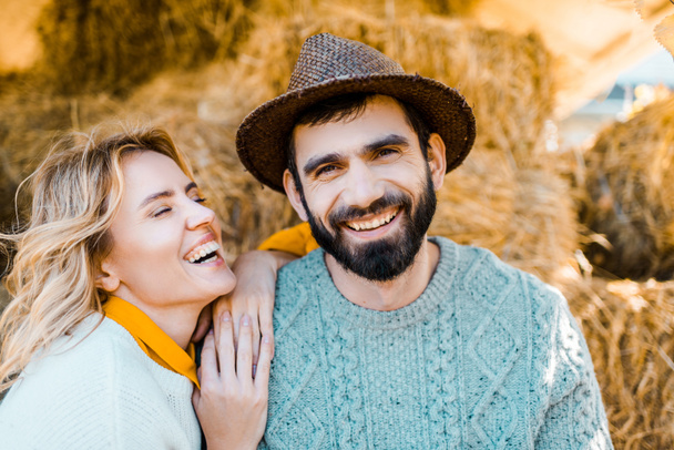 農家の農場で干し草のスタックの上に座ってのカップルを笑う  - 写真・画像
