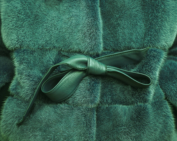 Fragment close up of a bright colorful green fur coat with leather bow. Beauty fashion theme. - Photo, Image
